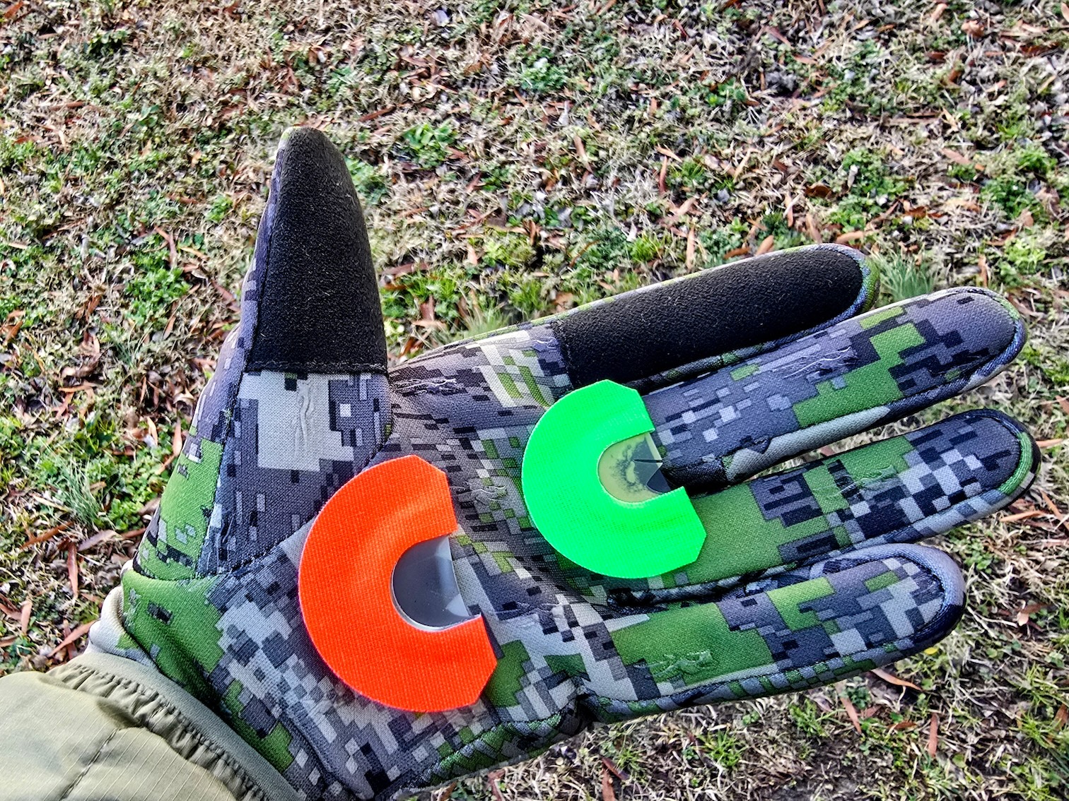 Two turkey mouth calls, one green and one orange, in the palm of a gloved hand. 