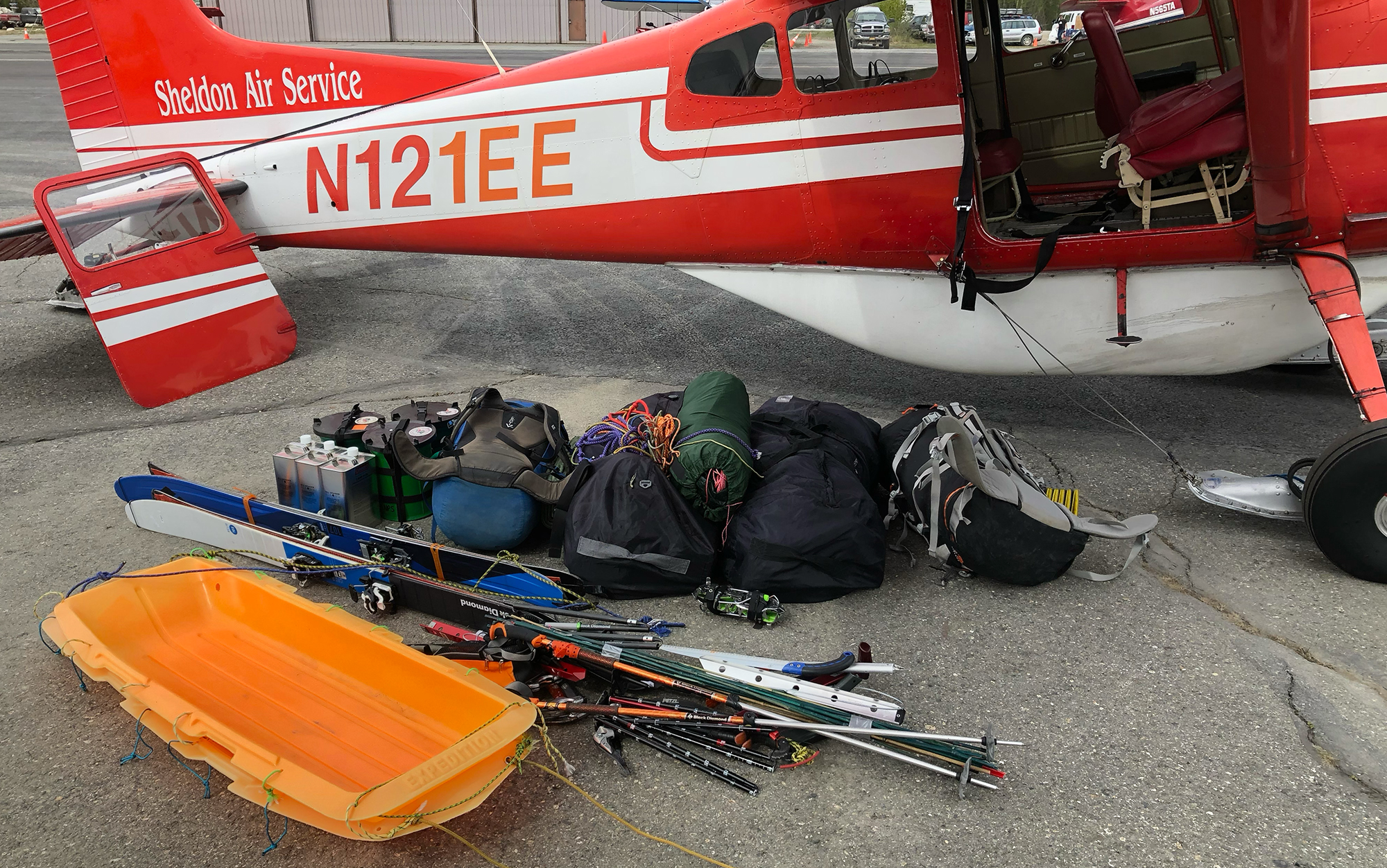 A pile of climbing and skiing gear sits in front of a plane.