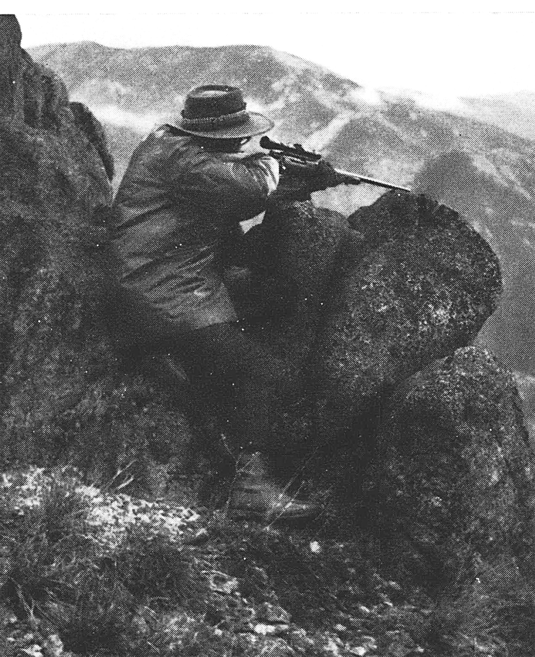 An old black and white photo of a woman resting her rifle on a rock.