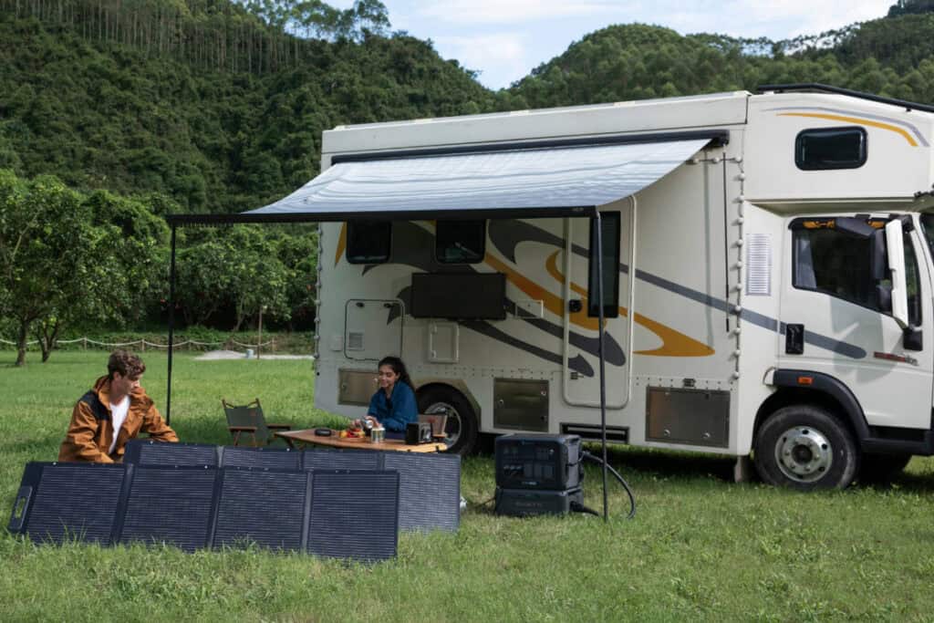 Class C motorhome set up in woody area with Bluetti reliable power solar generator set up under the extended awning