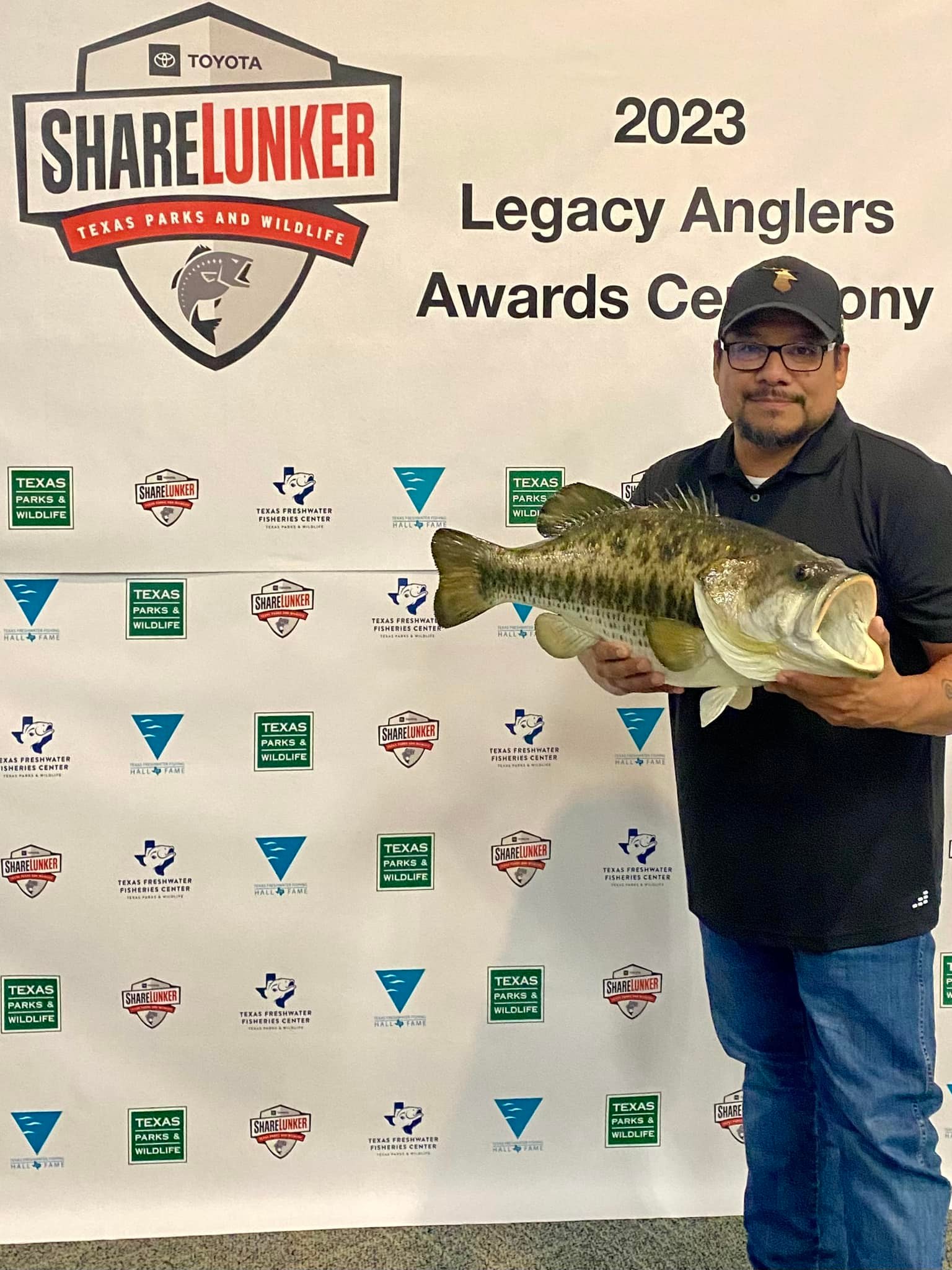 A man poses with a replica largemouth bass in 2023.