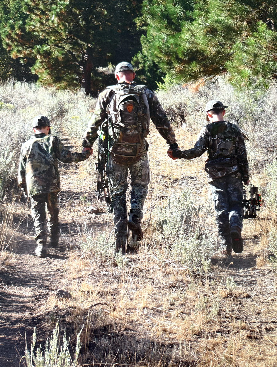 An elk hunter walks into the woods with his two sons.