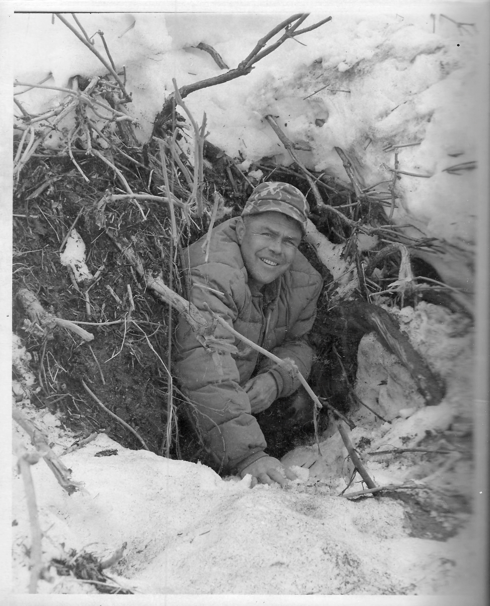 A vintage black and white photo of a bear biologist sticking his head out of a bear den.
