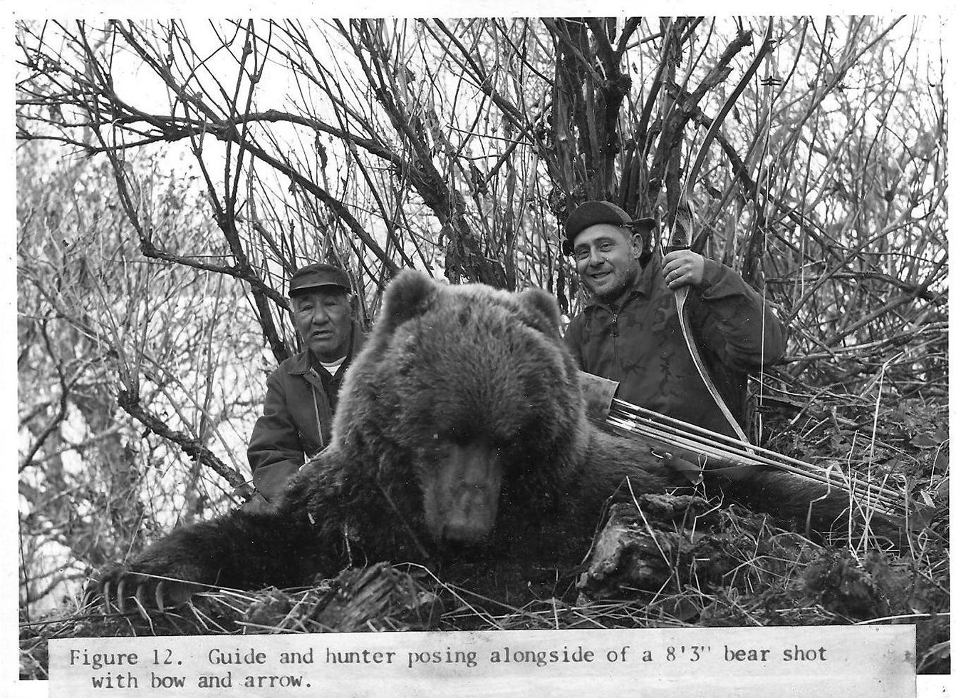 A vintage black and white photo of a bowhunter and his guide beside a big Kodiak brown bear.
