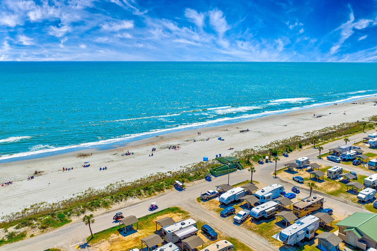 Aerial shot of RV park located adjacent to a sandy beach.