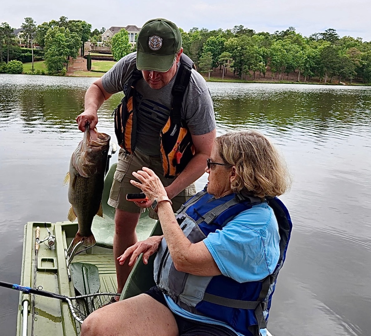 A man lips a largemouth bass and shows it to a woman in a boat.