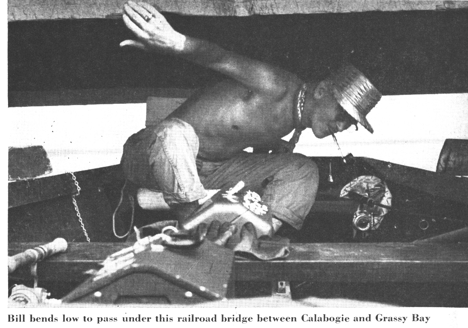 A man ducks under a bridge on a fishing boat in an old black and white photo