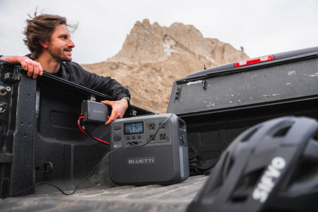 man turning on adapter to begin charging portable power station set in bed of truck