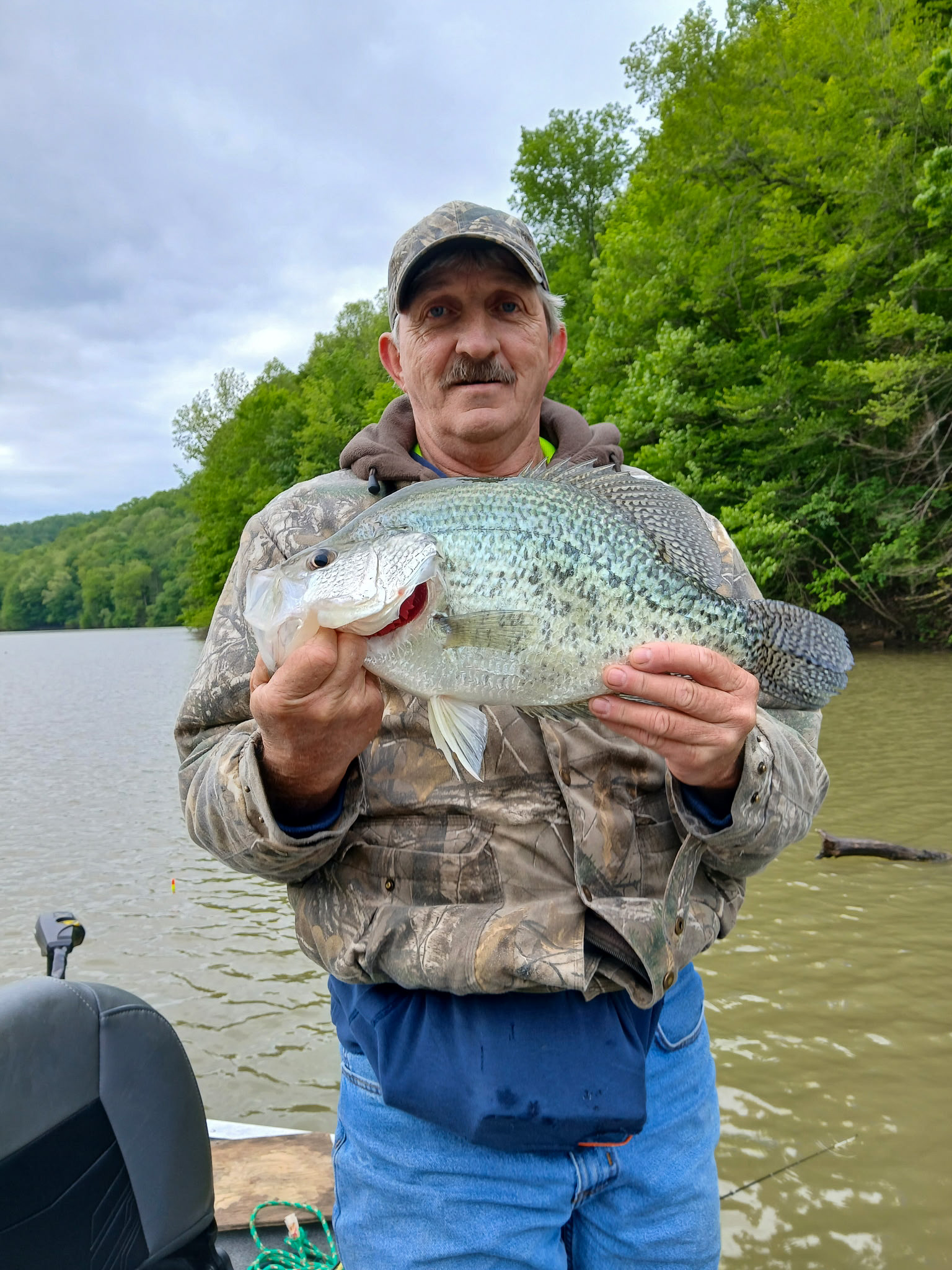 A man stands on a boat holding a black crappie up