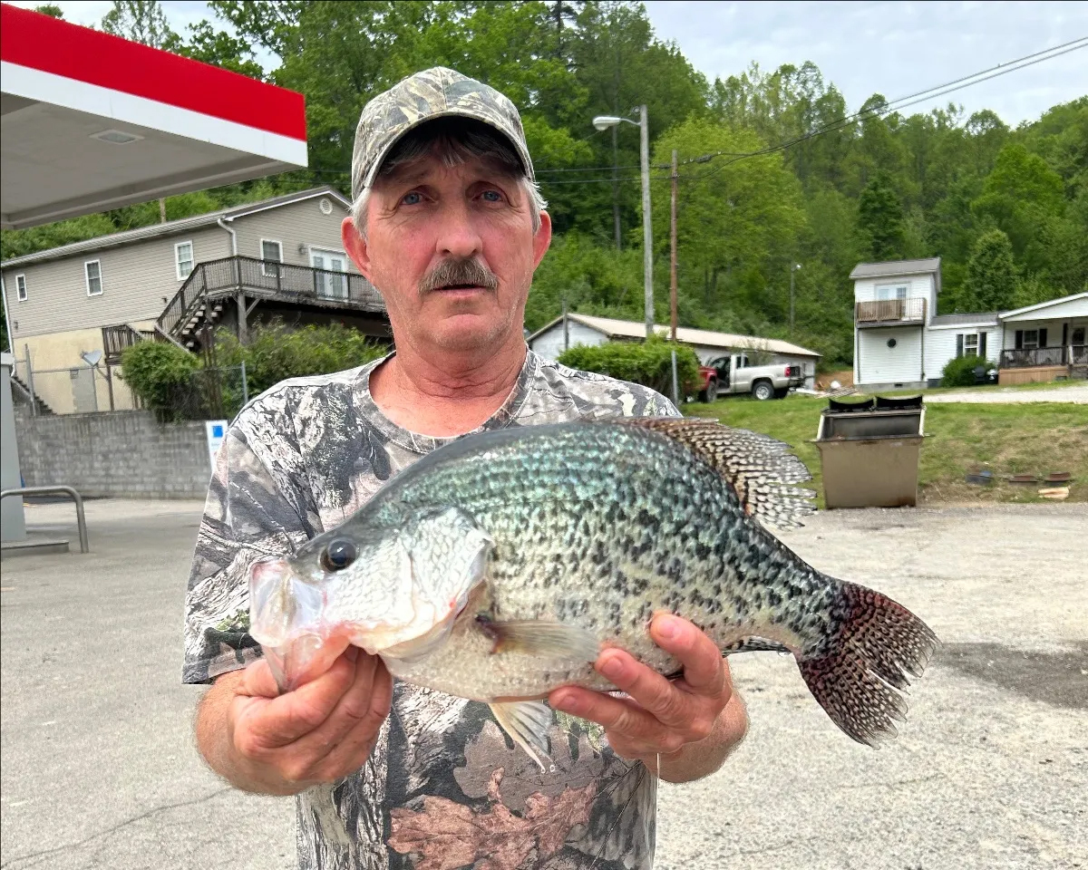 A man holds up a black crappie at a gas station