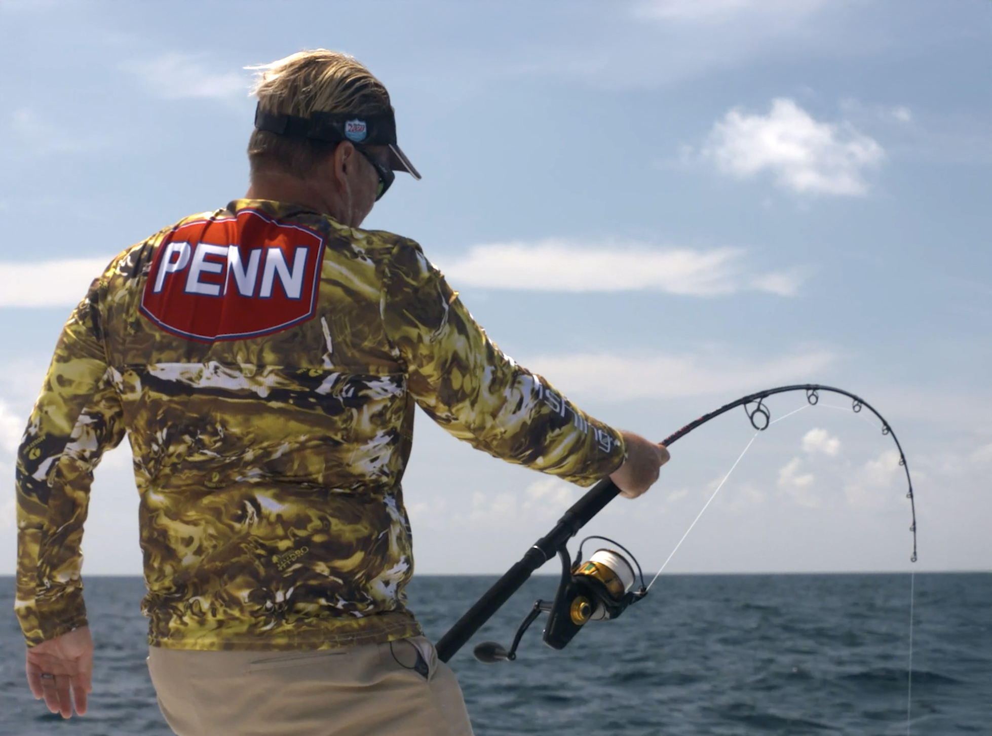 A man in a camo Penn fishing shirt holds one hand on a bent rod
