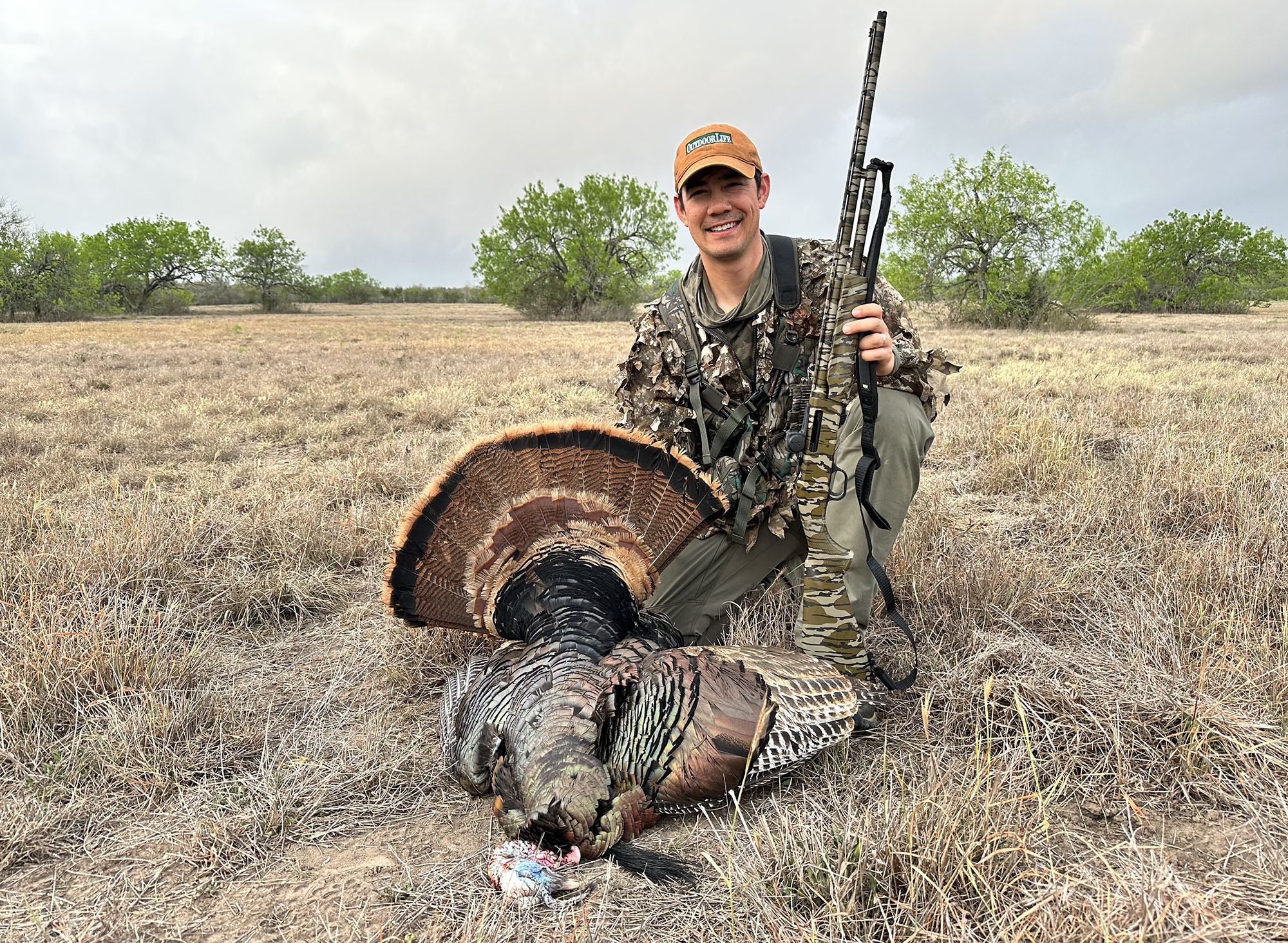 A turkey hunter with an orange hat and a dead bird