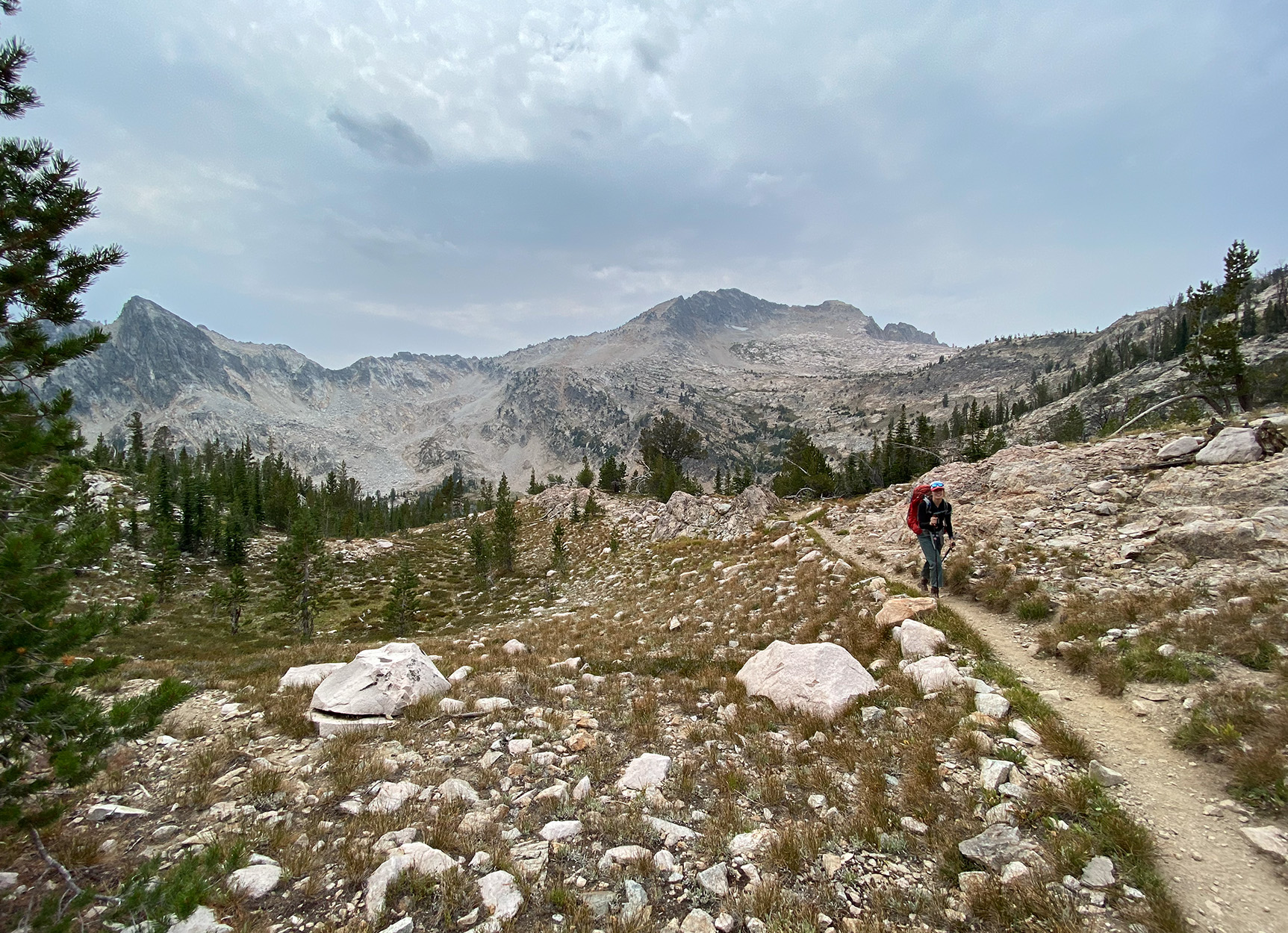A backpacker walks down a trail in the mountains.