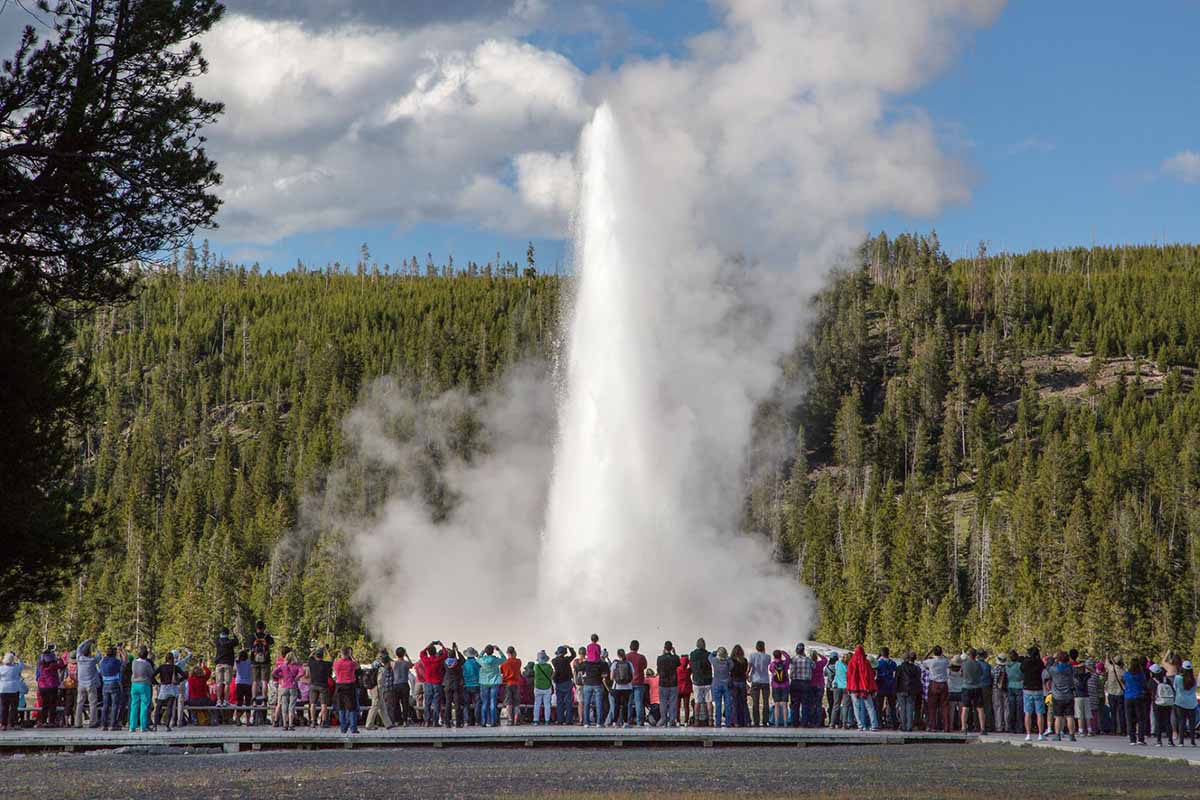 A crowd gathers in front of a steaming geyser.